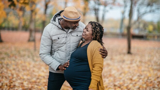 pregnant person and their partner outside in the fall
