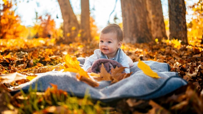 Cute baby girl on blanket at park on sunny autumn day