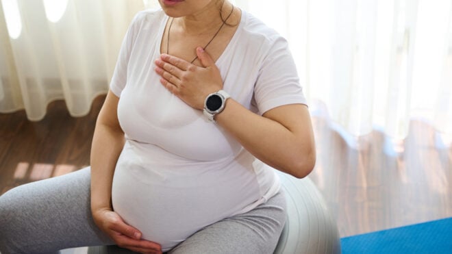 hypnobirthing, hypnosis birth, beautiful serene pregnant adult woman sitting on fitness ball, doing meditation and pranayama breathing exercises for healthy pregnancy, preparing body for childbirth, putting hands of chest and belly