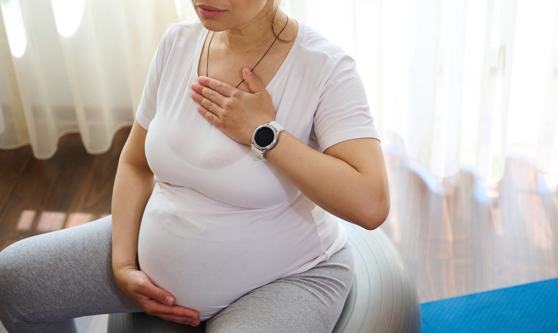 hypnobirthing, hypnosis birth, beautiful serene pregnant adult woman sitting on fitness ball, doing meditation and pranayama breathing exercises for healthy pregnancy, preparing body for childbirth, putting hands of chest and belly