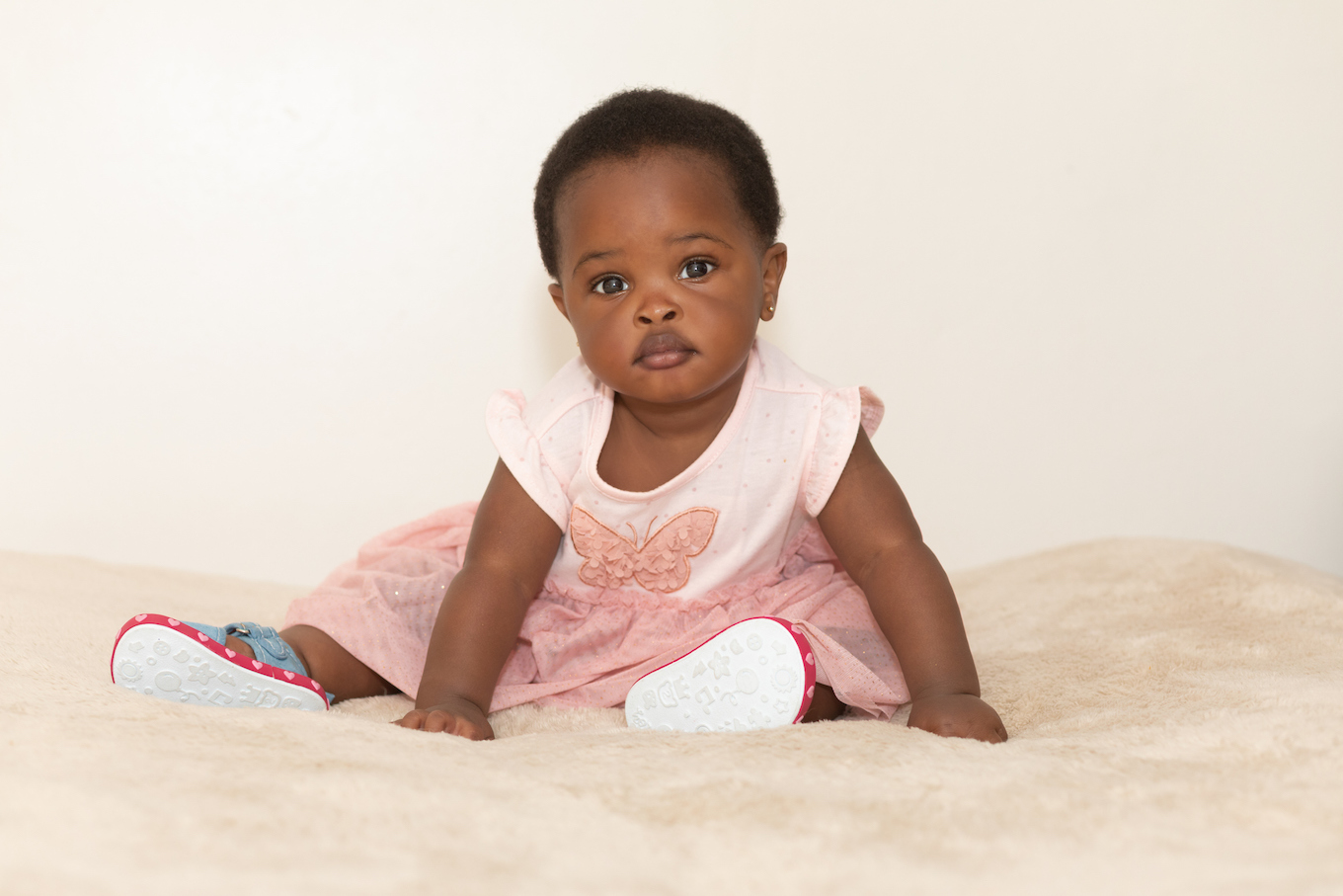 Portrait of a black baby girl dressed in pink sitting on a bed