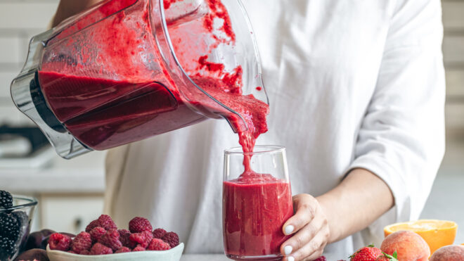 A woman making detox smoothie at home, woman pouring red smoothie to glass, healthy food concept.