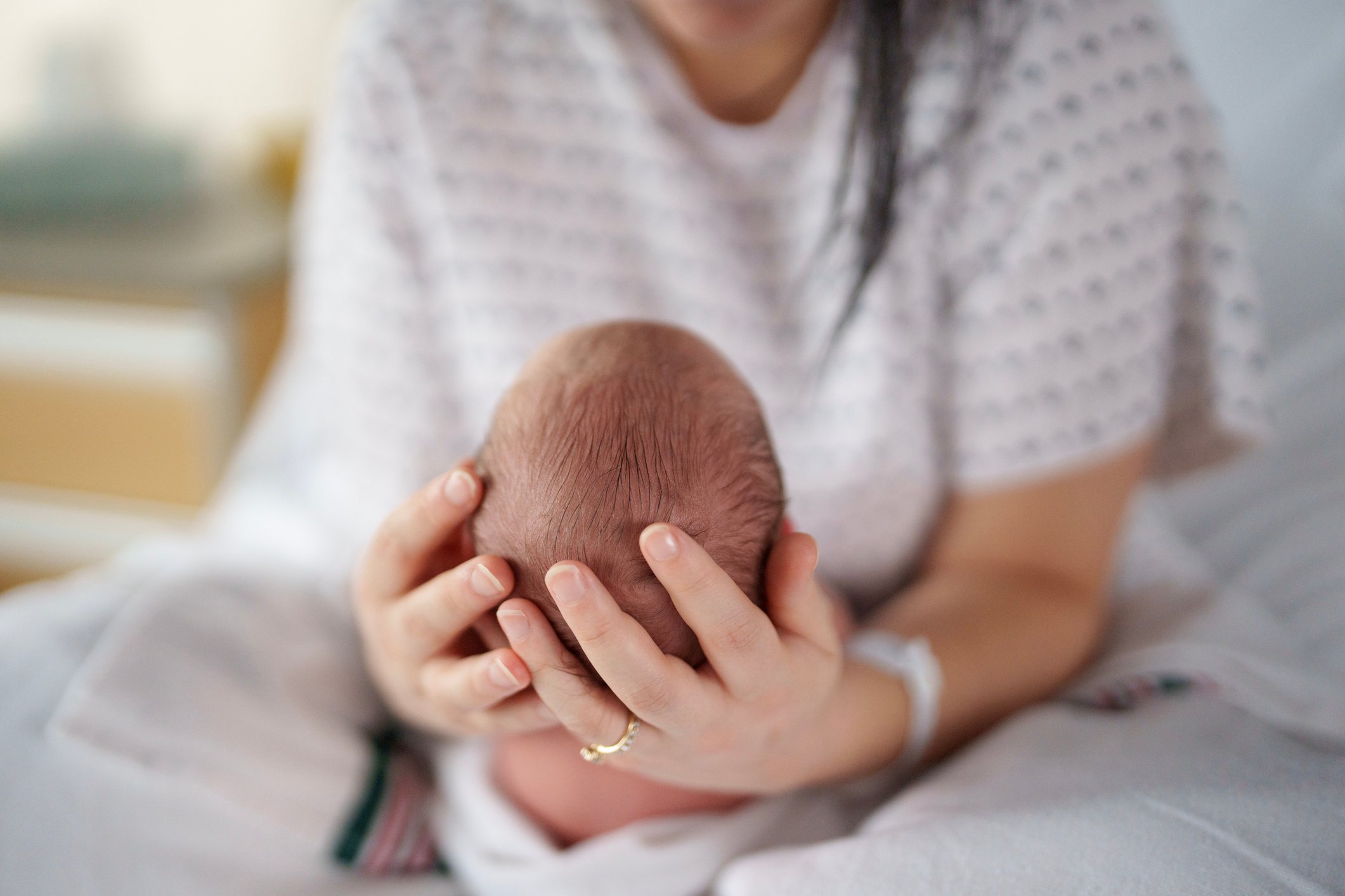 A woman gently holds her newborn baby out on her lap as she studies his features and enjoys some quite moments together in their hospital room alone.